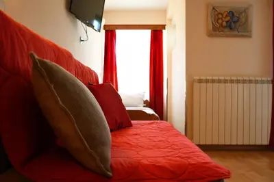 a red bed with red pillows and a window at Dental apartman in Vrnjačka Banja