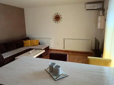 a living room with a table and a clock on the wall at Apartman Jasna in Vrnjci