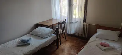 a room with two beds and a table and a window at Hostel Golub in Zaječar