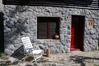 a stone house with a red door and a white chair at Studio za dvoje u Planinskoj kući Savić in Kopaonik