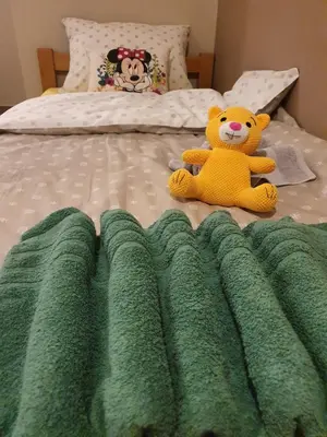 a teddy bear sitting on a bed with a green blanket at Guest House Jasmin in Niška Banja