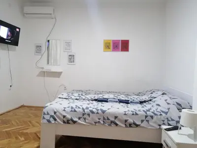 a white bedroom with a bed and a tv at Apartman Nana Jagodina in Jagodina