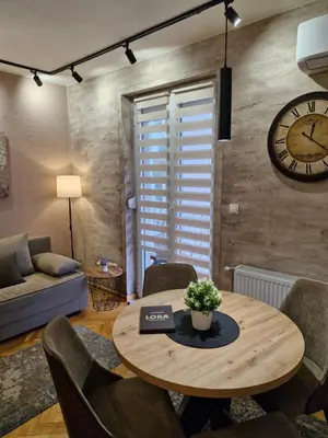 a living room with a table and a clock on the wall at Apartman Lora in Vrnjci