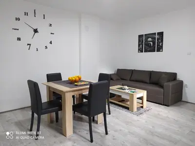 a living room with a table and a couch and a clock at Apartman Ljiljan in Soko Banja