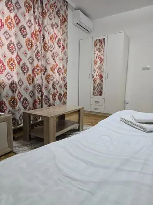 a bedroom with a bed and a table and curtains at Apartman Stefanovic in Vrnjačka Banja