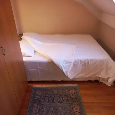 a small bedroom with a bed with white sheets and a rug at Loli Caffe Apartment in Prokuplje