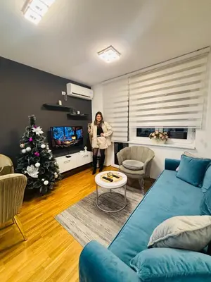 a woman standing in a living room with a blue couch at Apartman Korać in Vrnjačka Banja