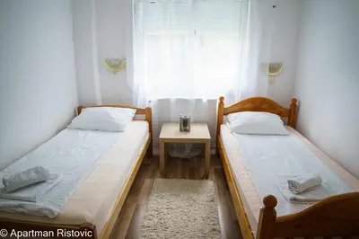 two beds in a room with a table and a window at Apartman Ristovic in Vrnjačka Banja