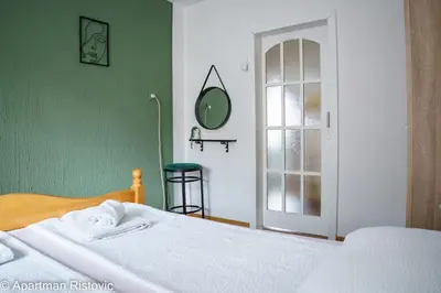 a bedroom with a white bed and a green wall at Apartman Ristovic in Vrnjačka Banja