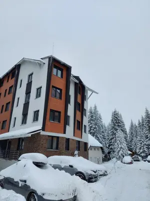 a building with cars parked in a parking lot covered in snow at Apartman Djordje-vila Montana in Kopaonik