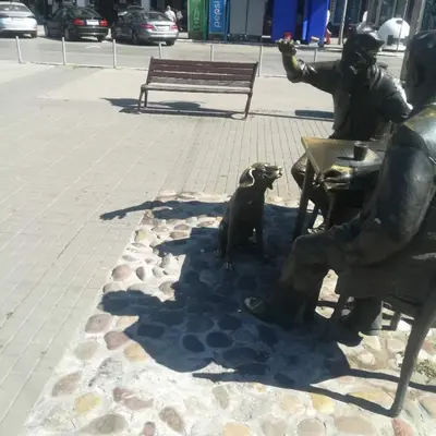 a statue of a man sitting on a bench with a dog at suvi centar in Niš