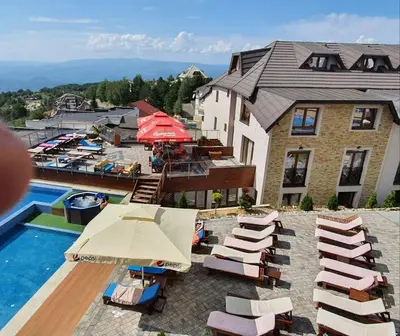 a pool with chairs and umbrellas next to a building at L&N Apartmani Kopaonik-Milmari Resort in Kopaonik