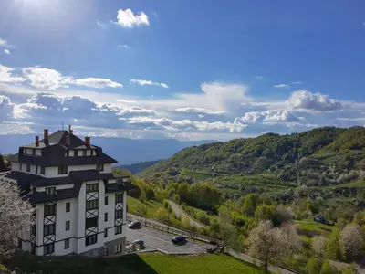 a building on a hill with mountains in the background at Ski & Spa Apartment N34 Milmari Resort Kopaonik in Kopaonik