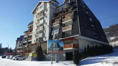 a large building in the snow with cars parked in front at Apartman Djole in Brzeće