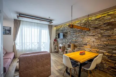 a living room with a table and a stone wall at Lux Apartman Lucky in Kopaonik