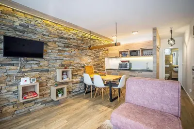 a living room with a table and a stone wall at Lux Apartman Lucky in Kopaonik