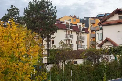 a large white building with trees in the background at Apartman 8 Extra Vrnjacka Banja in Vrnjačka Banja