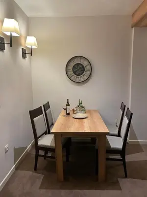 a dining room table with chairs and a clock on the wall at Luna Apartman, Župa Kopaonik in Kopaonik