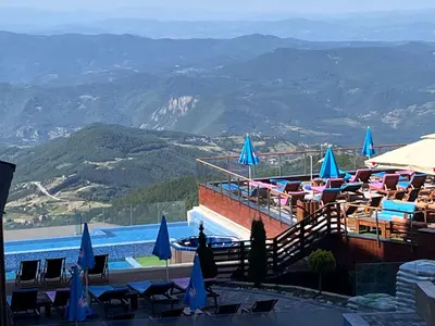 a swimming pool with chairs and umbrellas and mountains at Milmari P74, Quest apartmani, Kopaonik in Kopaonik