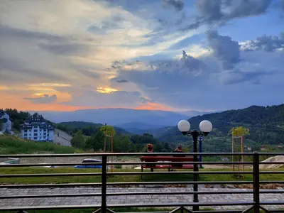 two people sitting on a bench looking at the mountains at N-delux apartman in Kopaonik