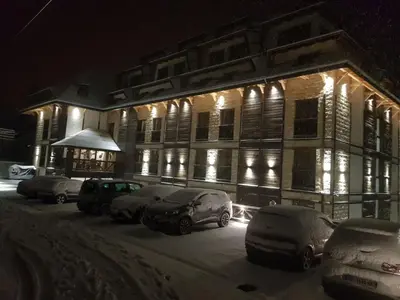 a snow covered building with cars parked in front of it at Apart Hotel & spa Zoned II, Kopaonik, apartman Lukač - special benifit Children up to 17 of age accompanied by two adutls staj for free! FREE PARKING! in Kopaonik