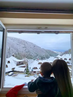 a woman and a child looking out of a window at Ski-in & Ski-out, Apartman Filip - 30m from GONDOLA Brzeće in Kopaonik