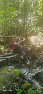 two people sitting on a bridge over a stream at Apt in the Sky - Kopaonik Kraljevi Čardaci in Kopaonik