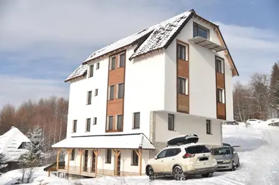 a large white building with two cars parked in the snow at Pegaz Premium Apartman Privatan Parking in Kopaonik