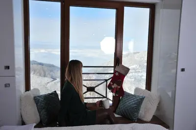 a woman sitting on a couch looking out of a window at Milmari N 20 Resort in Kopaonik