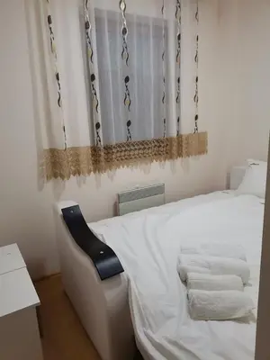 a bedroom with a white bed and a black chair at Apartmani Nedeljkovic Brzece Kopaonik in Brzeće