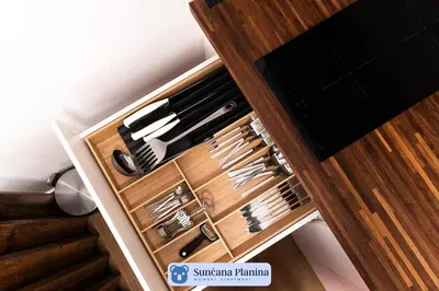 a drawer full of knives in a wooden cabinet at Sunčana Planina - Apartmani Wombat in Kopaonik