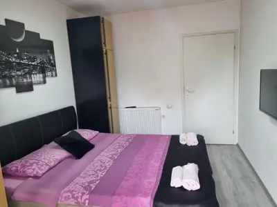 a bedroom with a bed with pink sheets and slippers at Family Apartmani Le in Leskovac