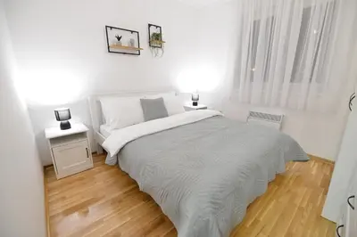 a white bedroom with a bed and a wooden floor at Apartman LUMI in Vrnjačka Banja