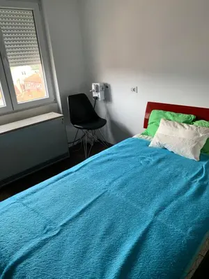a bedroom with a bed with a blue blanket and a chair at Aleksinac Centar in Aleksinac