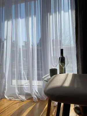 a window with white curtains and a bottle of wine at Apartman Nice in Vrnjačka Banja