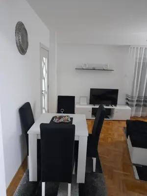 a white dining room with a white table and black chairs at Holiday apartments in Niš