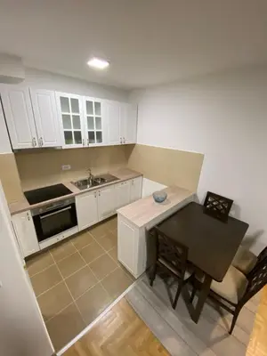 a kitchen with white cabinets and a table and a sink at Maya apartman sa dve spavace sobe in Vrnjačka Banja