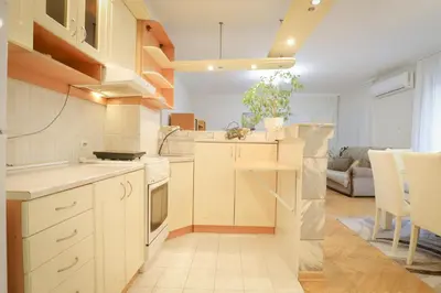 a kitchen with white cabinets and a living room at LOTUS (dvosoban apartman) in Vrnjačka Banja