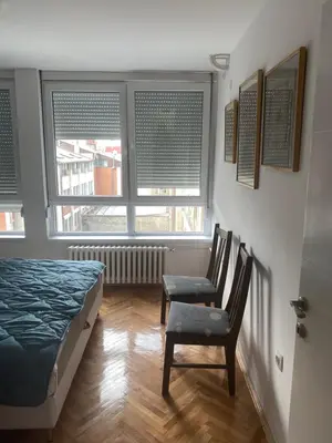 a bedroom with a bed and two chairs and two windows at Sandra in Niš