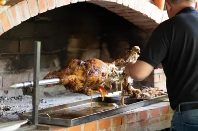 a man is cooking a chicken in an oven at Vila Dimitrijevic Lisine in Despotovac