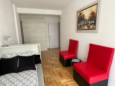 a bedroom with a bed and two red chairs at City Apartmani Niš in Niš