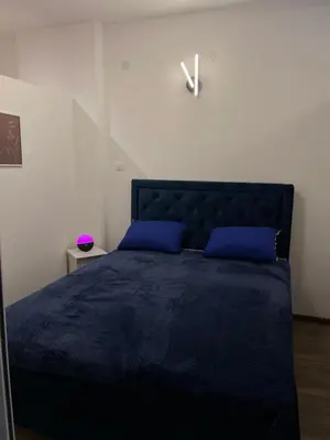 a bedroom with a blue bed with blue pillows and a clock at Enjoyment Apartment in Niš