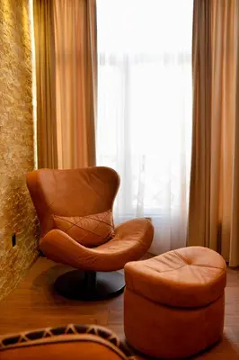 a brown chair and a stool in front of a window at Bella Superior Apartment in Kruševac
