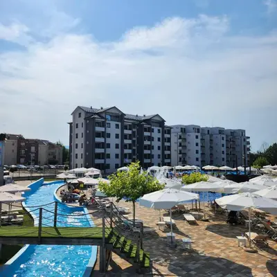 a pool with white umbrellas and chairs and buildings at Apartmani Sunlight in Vrnjačka Banja