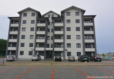 a large white building with cars parked in a parking lot at Neda Lux Apartmani 5 nocenja, šesto gratis in Vrnjačka Banja