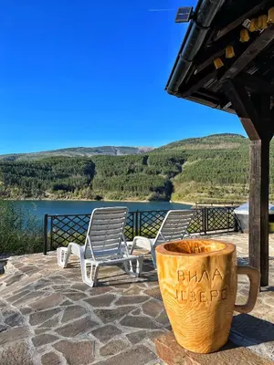 two chairs and a coffee cup on a patio with a lake at Zavojsko jezero - Vila Jezero in Pirot