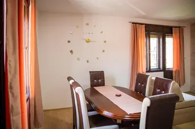 a dining room table and chairs with a clock on the wall at Beli Ocnjak in Soko Banja