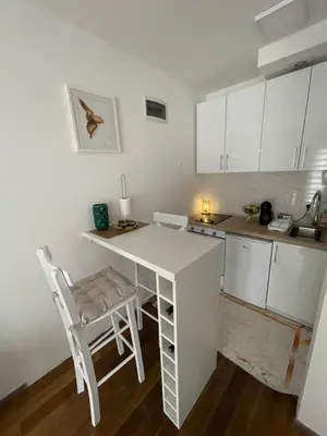 a white kitchen with a table and a chair at Apartman 5 Vrnjačka Banja in Vrnjačka Banja