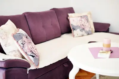 a purple couch with pillows and a white table at Apartman Provansa in Vrnjačka Banja