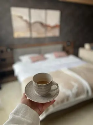 a person holding a cup of coffee in front of a bed at Apartman Kopaonik Woodside 106 in Kopaonik